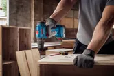 O persoană purtând echipament de siguranță găurește o placă de lemn într-un atelier.