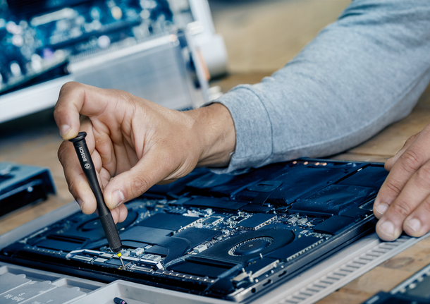 Persoană care folosește o șurubelniță pentru a repara placa de bază a unui laptop.