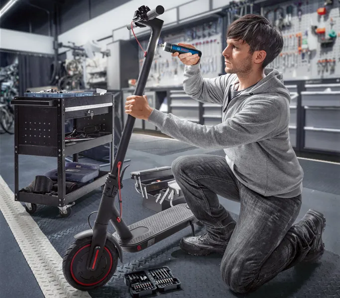 O persoană repară o trotinetă electrică folosind o șurubelniță fără fir într-un atelier.