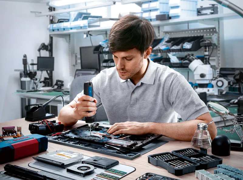 O persoană folosește o șurubelniță fără fir pentru a asambla componente electronice pe o bancă de lucru.