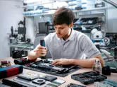 O persoană folosește o șurubelniță fără fir pentru a asambla componente electronice pe o bancă de lucru.