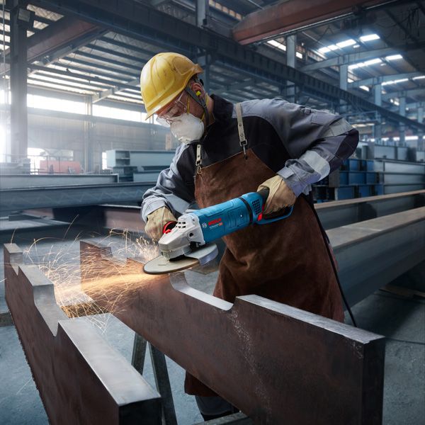 O persoană care poartă echipament de siguranță șlefuiește o grindă de oțel, producând scântei într-o fabrică.