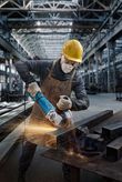 O persoană care poartă echipament de siguranță șlefuiește grinzi metalice, producând scântei strălucitoare.