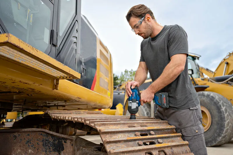 O persoană care poartă echipament de siguranță folosește o cheie de impact fără fir pe șenila unui excavator.