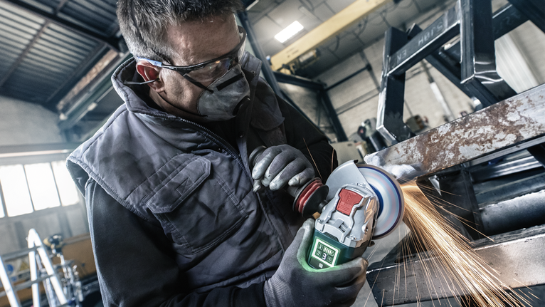 O persoană care poartă echipament de siguranță șlefuiește o grindă metalică, producând scântei strălucitoare.