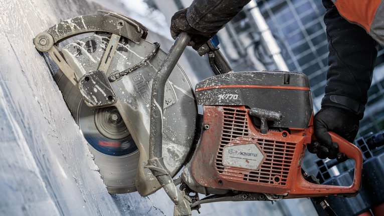 O persoană care poartă echipament de siguranță operează un ferăstrău electric mare pentru a tăia beton.