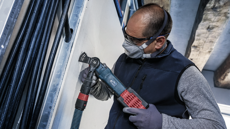 O persoană purtând echipament de siguranță taie gips-carton cu o unealtă electrică.