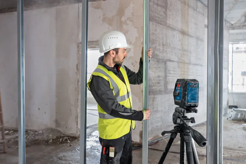 O persoană care poartă echipament de siguranță aliniază știfturi metalice folosind un instrument de nivelare cu laser.