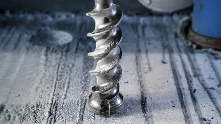 Un burghiu mare cu spirală face o gaură într-o suprafață de beton.