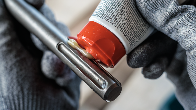 O persoană care poartă echipament de siguranță aplică lubrifiant pe o unealtă metalică.