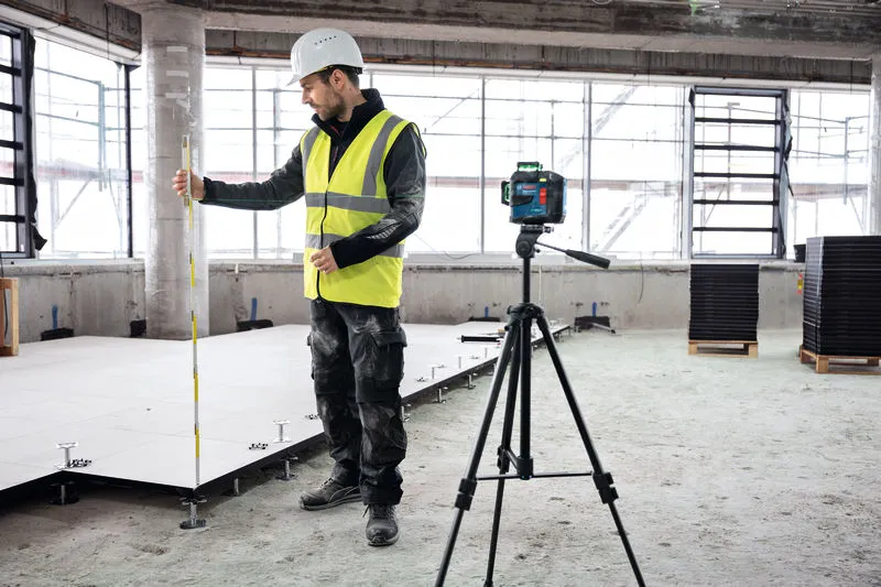 O persoană care poartă echipament de siguranță folosește un instrument de nivelare cu laser pe un șantier.