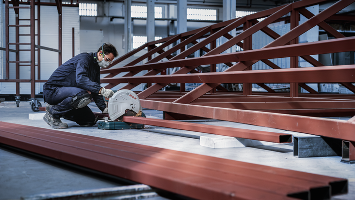 O persoană purtând echipament de siguranță taie o grindă de oțel într-un depozit industrial.