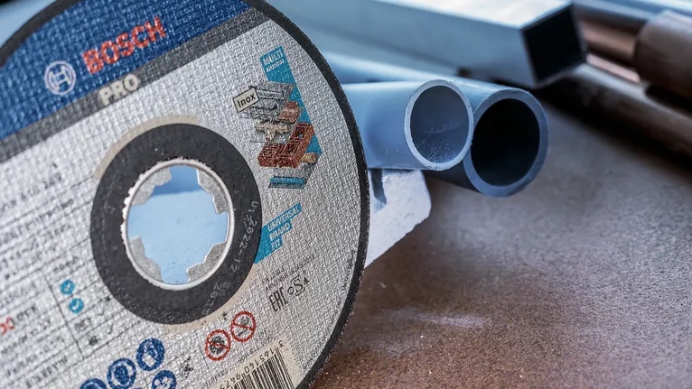 Disc de tăiere așezat pe o bancă de lucru lângă mai multe țevi de plastic.