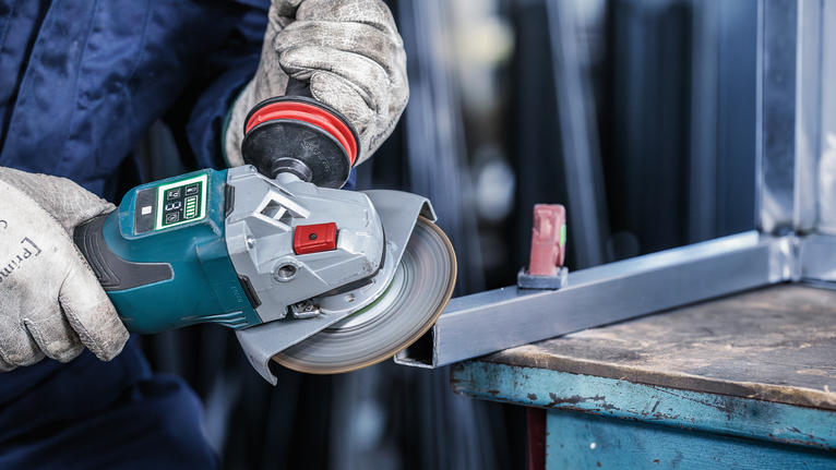 Persoană purtând echipament de siguranță șlefuiește o structură metalică cu un polizor unghiular.