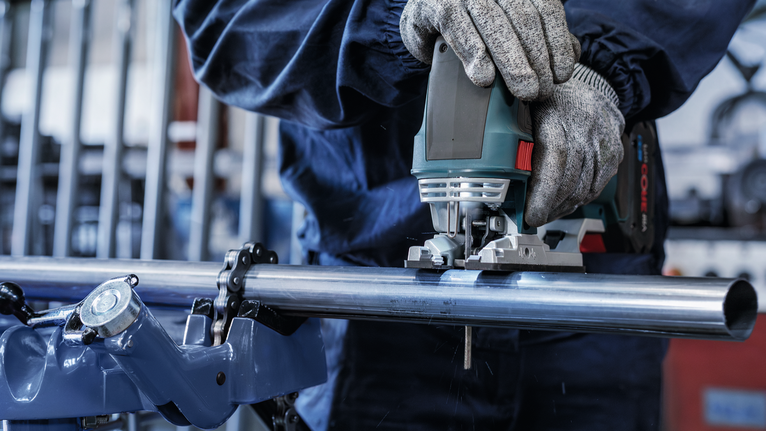 Persoană care poartă echipament de siguranță folosește un ferăstrău vertical pentru a tăia o țeavă metalică.