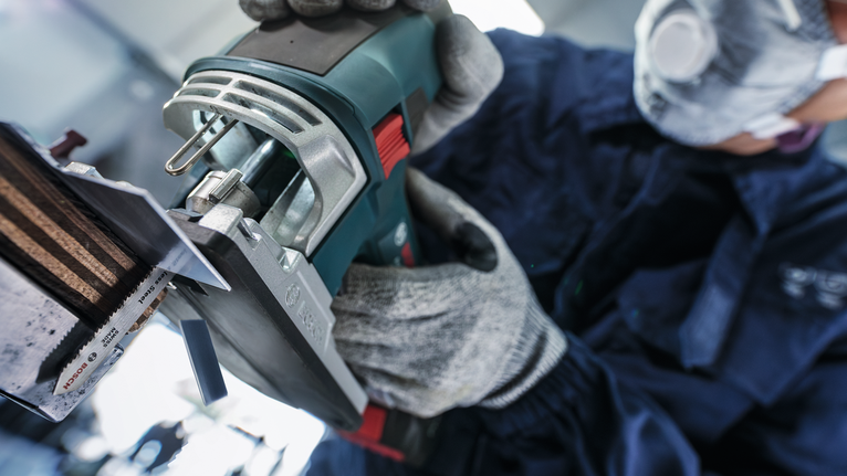 O persoană care poartă echipament de siguranță operează o unealtă electrică pentru a tăia o piesă metalică.