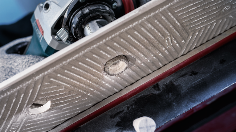 O persoană purtând echipament de protecție găurește o gaură într-o țiglă cu o unealtă electrică.