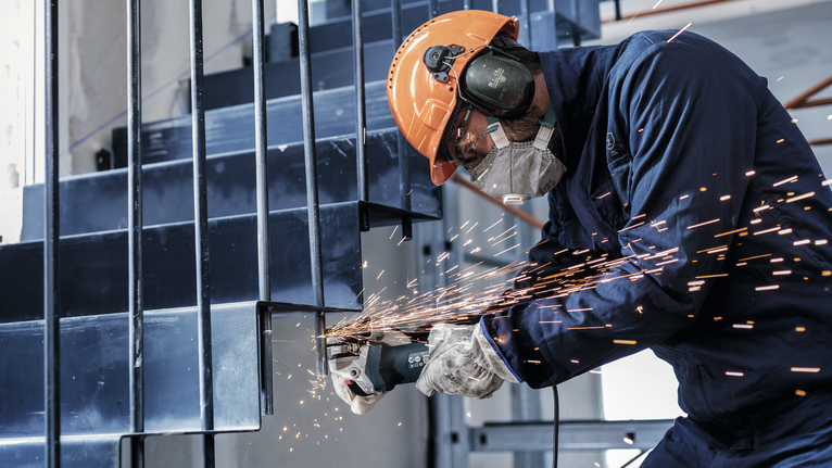 Persoană purtând echipament de siguranță scrâșnește o scară metalică, trimițând scântei spre exterior.