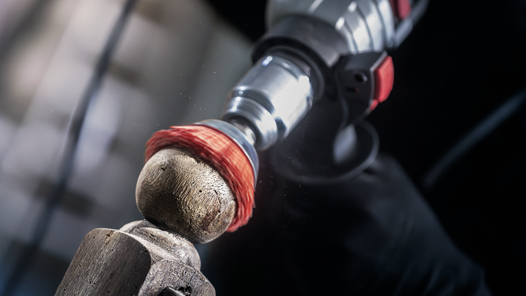 Persoană care folosește o unealtă electrică cu o perie de sârmă pentru a curăța o suprafață de lemn.