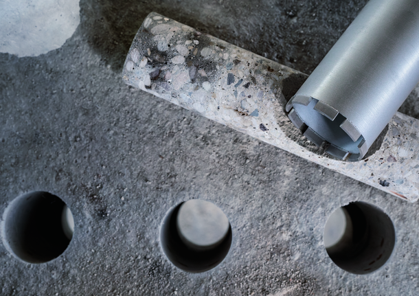 Carotă și un cilindru de beton lângă găuri proaspăt forate într-o placă de beton.