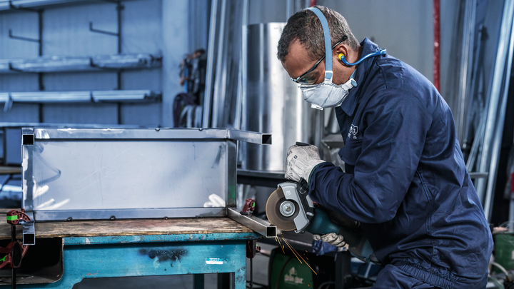 Persoană purtând echipament de siguranță taie tablă metalică cu un polizor unghiular.