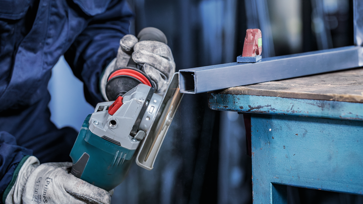 Persoană care poartă echipament de siguranță folosește o polizor unghiular pentru a tăia o grindă metalică.