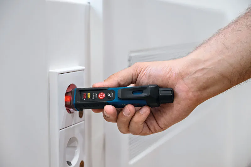 O persoană folosește un tester de tensiune fără contact lângă o priză electrică.