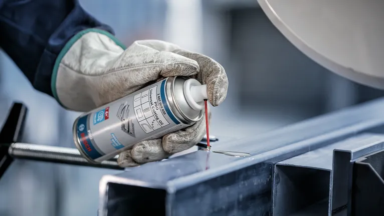 O persoană care poartă echipament de siguranță pulverizează lubrifiant pe o grindă metalică.