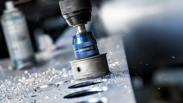 Fierăstrău circular care găurește găuri circulare într-o tablă metalică, cu așchii metalice împrăștiate în jur.