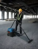 O persoană care poartă echipament de siguranță folosește un aspirator umed-uscat pentru a curăța podeaua unui șantier de construcții.