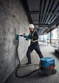 O persoană purtând echipament de siguranță găurește un perete de beton folosind un extractor umed și uscat.