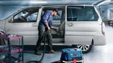 O persoană care poartă echipament de siguranță folosește un extractor umed-uscat pentru a curăța interiorul unei mașini.