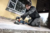 O persoană purtând echipament de siguranță șlefuiește o suprafață de beton cu o unealtă electrică.