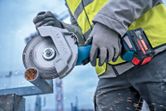 O persoană care poartă echipament de siguranță taie o țeavă metalică cu un polizor unghiular fără fir.