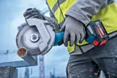 O persoană care poartă echipament de siguranță taie o țeavă metalică cu un polizor unghiular fără fir.