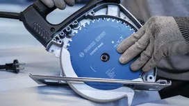 Persoană purtând echipament de siguranță fixează o lamă de ferăstrău circular într-o unealtă electrică.