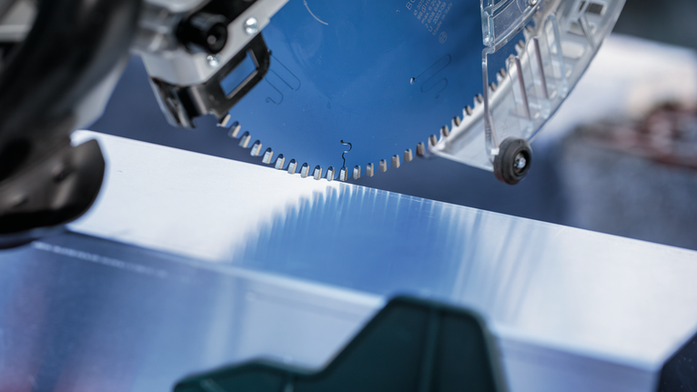 Lamă de ferăstrău circular care taie printr-o suprafață metalică strălucitoare.