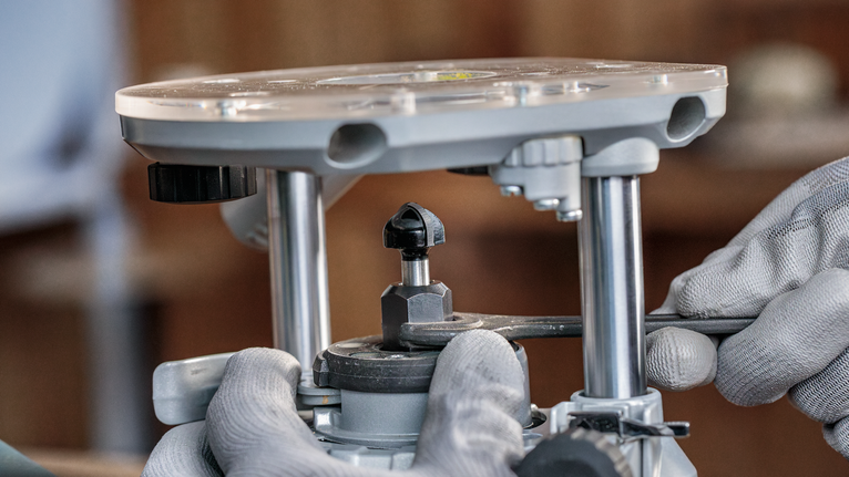 Persoană purtând echipament de siguranță ajustează o unealtă de frezat folosind o cheie.