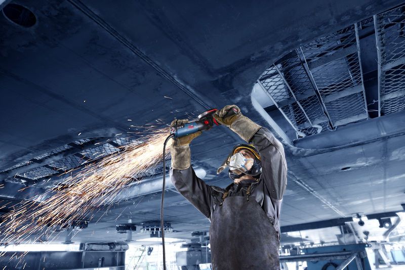 O persoană care poartă echipament de protecție macină metalul deasupra capului, creând o ploaie de scântei.