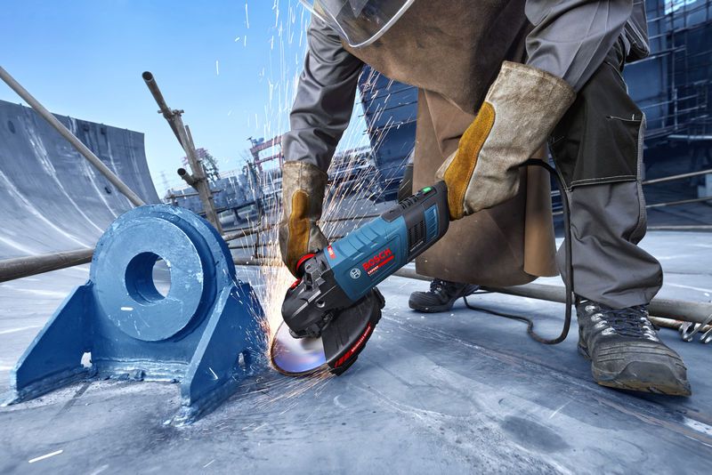 O persoană care poartă echipament de siguranță șlefuiește metalul cu o unealtă electrică, producând scântei.