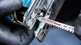O persoană care poartă echipament de siguranță introduce o lamă de fierăstrău pendular într-o unealtă electrică.