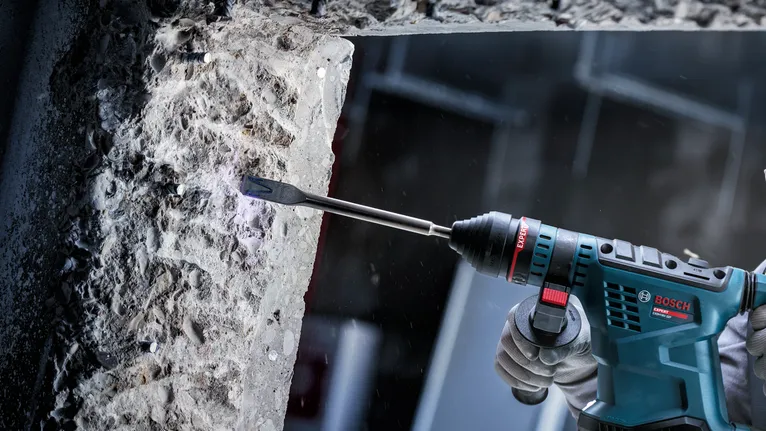 Persoană care poartă echipament de siguranță folosește o unealtă electrică pentru a ciobi betonul.