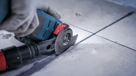 Persoană purtând echipament de siguranță taie o țiglă cu o polizor unghiular.