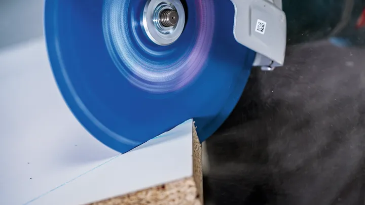 Lamă de ferăstrău circular care taie printr-o placă de lemn laminată.