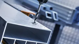 Un burghiu creează o gaură într-o grindă metalică într-un mediu industrial.