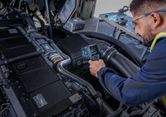 O persoană care poartă echipament de siguranță folosește un termodetector pentru a verifica temperatura motorului.
