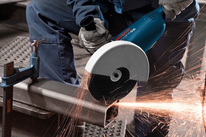 O persoană care poartă echipament de siguranță taie o țeavă metalică cu o polizor unghiulară, creând scântei.