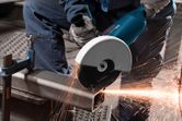 O persoană care poartă echipament de siguranță taie o țeavă metalică cu o polizor unghiulară, creând scântei.