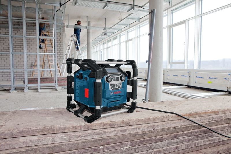 Radio de la locul de muncă conectat pe niște scânduri de lemn, cu două persoane pe scări în fundal.