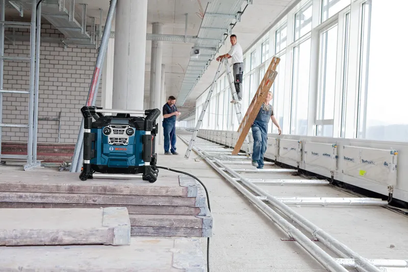 Muncitori în construcții care poartă echipament de siguranță instalează scări într-o clădire luminoasă, dotată cu un radio de șantier.